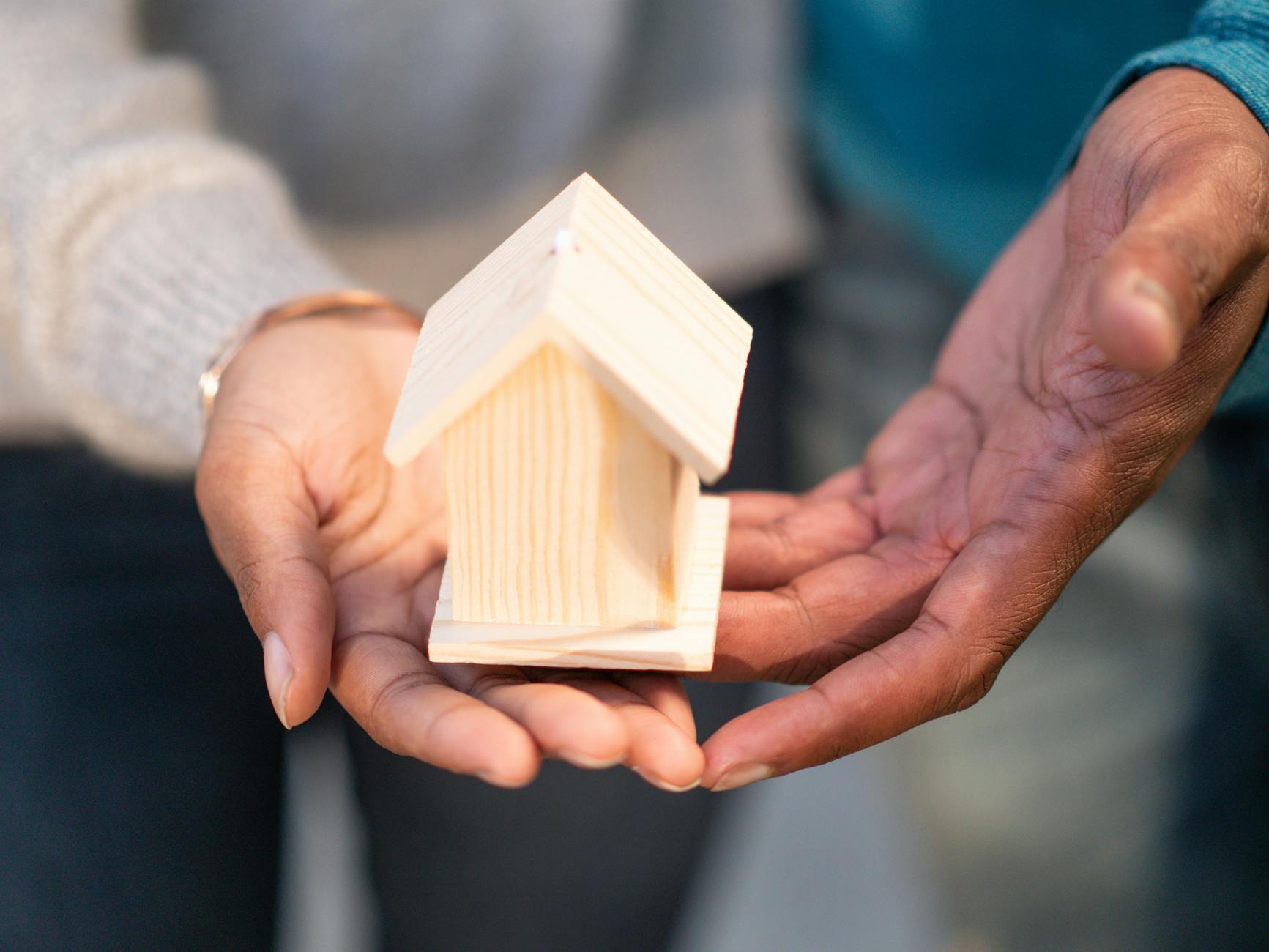 people holding miniature wooden house